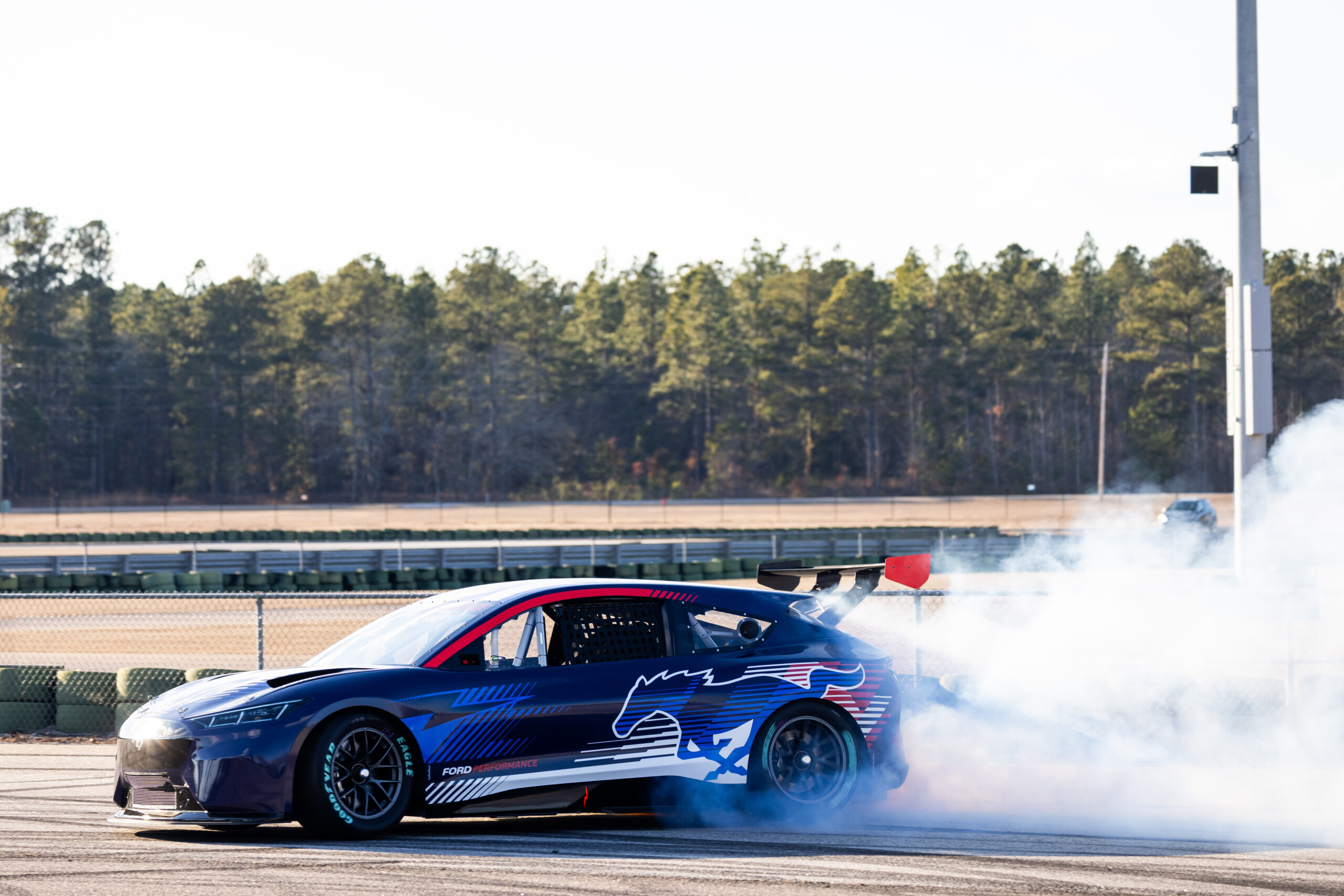 The low, wide stance and large rear wing of the Mustang Mach-E racer enhance its performance and aesthetic appeal.